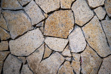 Textured stone wall with cracked, angular pieces and warm earthy tones.