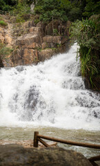 Rushing waterfall cascades over rocky terrain, surrounded by lush greenery.