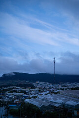 A serene twilight view of a town with greenhouses under a blue sky and distant mountains.