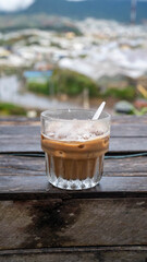 Chilled coffee drink in a glass, set against a blurred outdoor background.