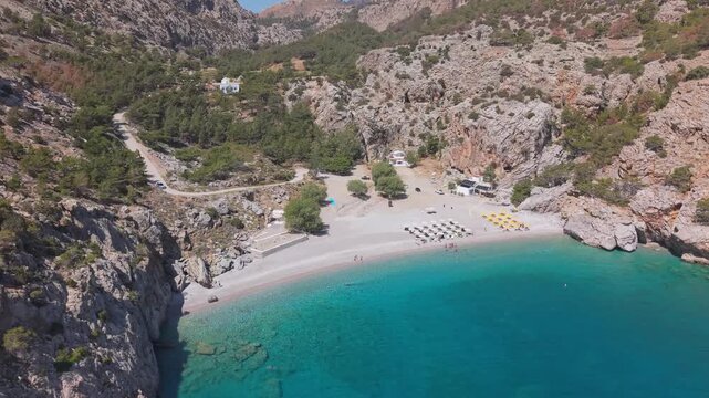 Aerial drone shot captures the crystal-clear waters of a Karpathos beach while gradually revealing the Achata landscape in the background.