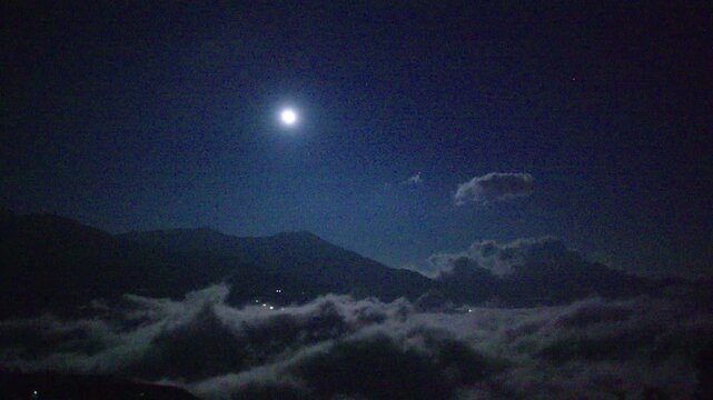 Full moon shining above sea of clouds over mountain landscape