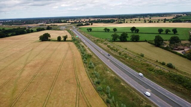 Norfolk dual carriageway through country fields just outside Norwich. The Broadland Northway with a small amount of vehicles travelling along during the day captured by aerial footage.