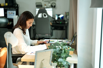 Female graphic designer working on logo creation with drawing tablet and color palette in modern bright office.