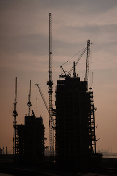 Construction site with large tower cranes against a sunset sky. Vertical image