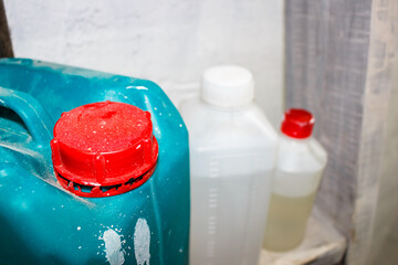 Vibrant red cap on a teal plastic jerrycan with white speckles, set against blurry background of other chemical containers