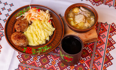 Traditional Ukrainian lunch with mashed potatoes, meat cutlets and soup on embroidered tablecloth