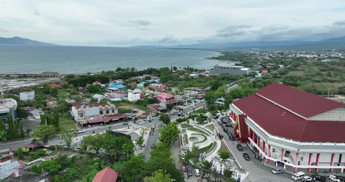 Aerial view of Palu Bay showing coastline, residential areas, green landscapes, and distant mountains under cloudy skies.
