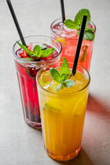 Three vibrant drinks with mint leaves sit invitingly on a table, perfect for a warm afternoon