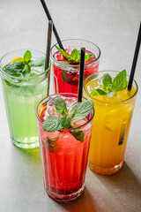Four colorful drinks with mint leaves on top sit on a table, capturing the essence of summer