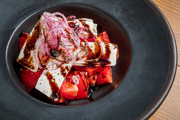 Colorful bowl of feta cheese and tomatoes garnished with red onions and balsamic glaze