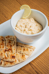 Creamy hummus served in a bowl alongside warm, toasted flatbread and a lemon wedge