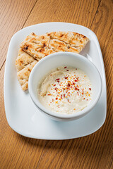 Creamy dip topped with spices is paired with warm flatbread on a simple plate, inviting enjoyment