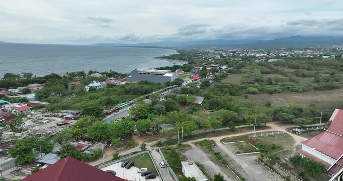 Aerial view of Palu Bay showing coastline, residential areas, green landscapes, and distant mountains under cloudy skies.