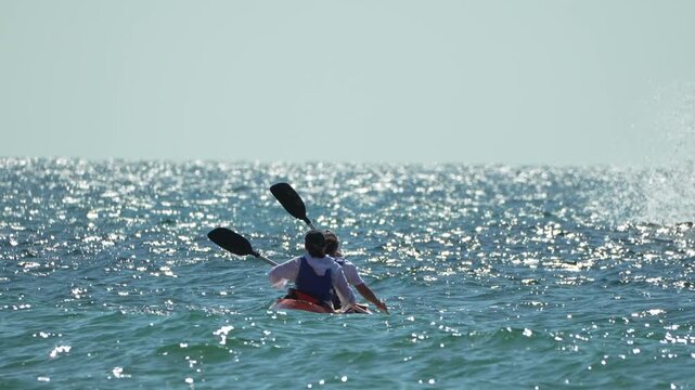 Kayaking ocean water, two people paddling a tandem kayak on sparkling blue sea under clear sky