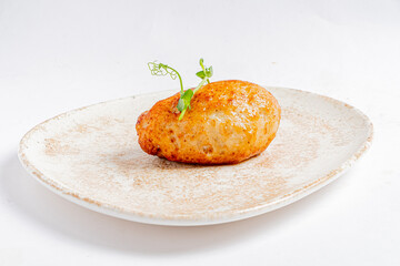 A beautifully golden potato dumpling sits on a textured plate, topped with fresh green herbs