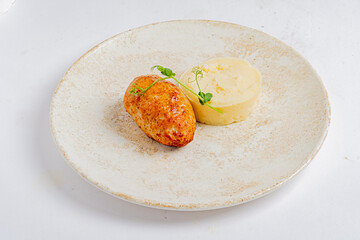 A tender roasted protein item sits beside a mound of creamy mashed potatoes, garnished artistically