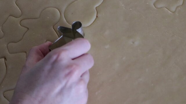A close up of a small cookie in the shape of a girl being cut out of a sheet of cookie dough for Christmas cookies.