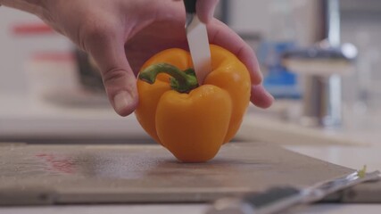 Close up of the core of yellow pepper being removed to prepare for cooking. Shot in slow motion in modern kitchen over a cutting board.