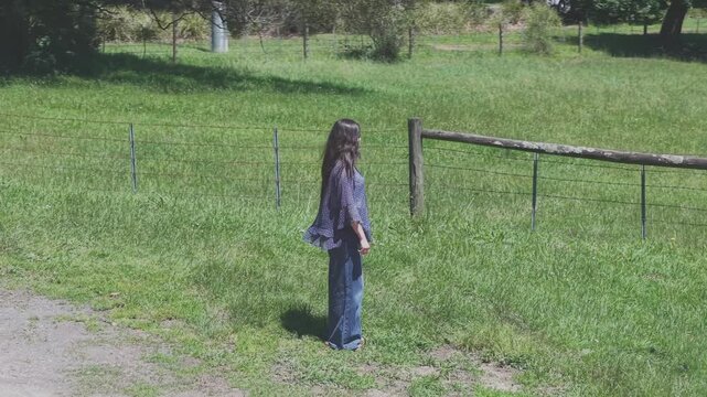 Serene shot of a woman standing in a lush green field by a rustic wooden fence. Captures calm, natural beauty, and the peacefulness of the countryside under soft daylight in Silvan.