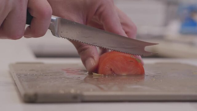 A close up of a juicy roma tomoto being sliced on a cutting board in a modern kitchen.