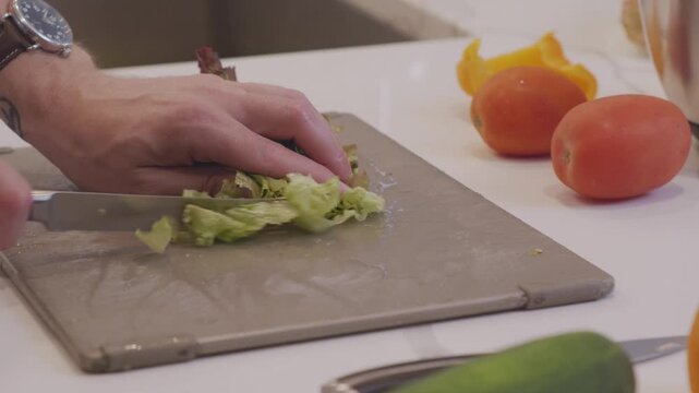 A close up of lettuce being chopped in preparation of a salad. Shot in a modern kitchen surrounded by kitchenware and vegetables.