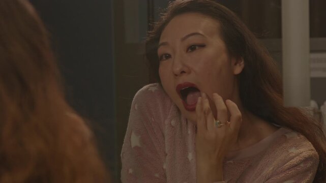A beautiful Asian lady adjusts her lipstick with her finger and gives a kiss to the mirror. The woman winks and sensually walks away.