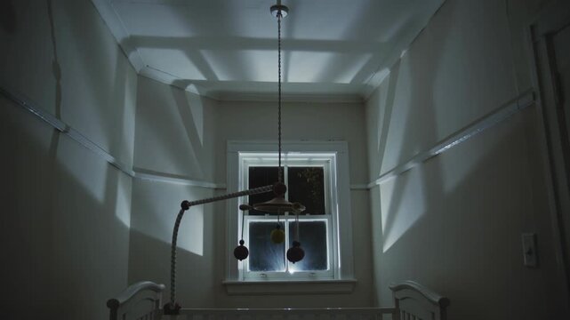 Nursery crib and mobile in a baby room with moonlight shadows movement across the walls