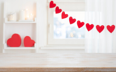 Light blurry window interior background decorated with red hearts and bleached wooden table top in front