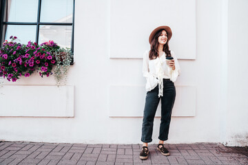 Lifestyle portrait of young stylish woman dressed in white blouse. Model walking with coffee cup in...