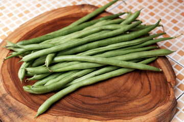 Freshly green beans arranged on a wooden cutting board create an appealing display against a table background, perfect for highlighting healthy eating