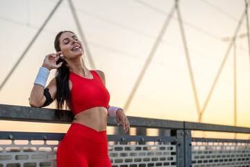 Smiling woman in red workout attire enjoys sunset on urban bridge during evening jog