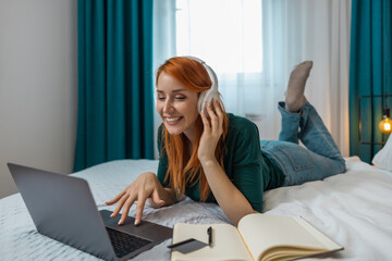 Woman enjoying music while studying on her laptop in a cozy bedroom during the day