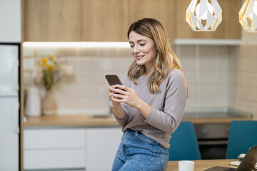 Young woman using smartphone while standing in modern kitchen with bright decor