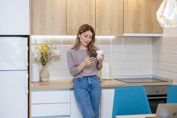 Young woman checks phone while enjoying coffee in modern kitchen during day