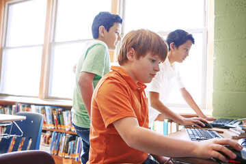 Boy, children and learning in school with computer for digital literacy, education and skill development. Kid, classmates and browsing with desktop in library for homework, knowledge and research.