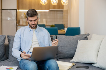 Man working on a laptop while holding a smartphone in a modern living room setting