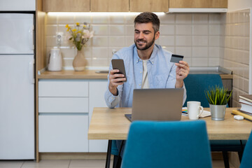 Man using smartphone and credit card while shopping online in cozy kitchen space