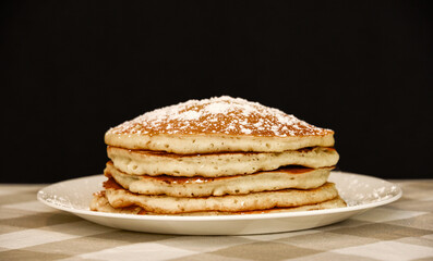 A stack of five golden brown pancakes with powdered sugar.