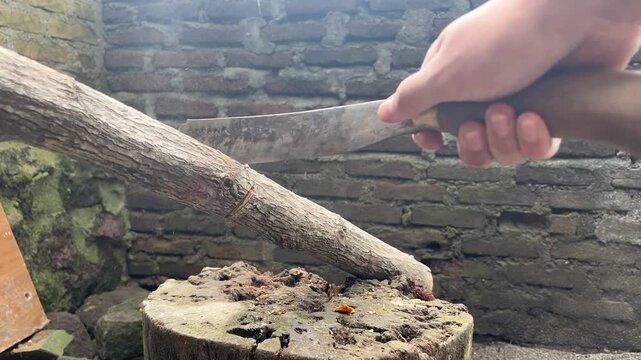 Detailed footage of hands holding a machete and repeatedly chopping wood. The focus on the swinging motion conveys a sense of power, precision, and a realistic physical work process.