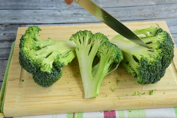 cutting fresh broccoli with knife on wooden board