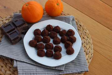 Dark Chocolate truffles candies with candied orange pells on white ceramic plate on wooden table