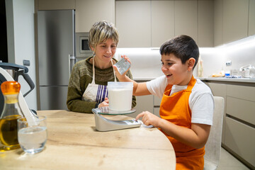 Mother and son enjoying baking together in a modern kitchen. Boy learning to weigh flour on a digital scale