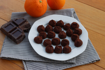 Dark Chocolate truffles candies with candied orange pells on white ceramic plate on wooden table