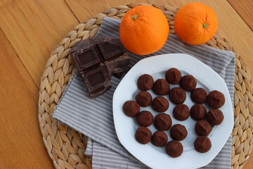 Dark Chocolate truffles candies with candied orange pells on white ceramic plate on wooden table