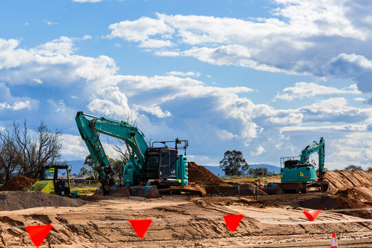 Excavator digging in dirt on worksite during construction of bypass for rural town