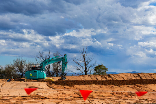 Excavator digging in dirt on worksite during construction of bypass for rural town