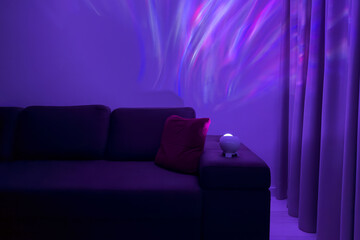 Cozy living room with modern couch, colorful ambient lighting of projector, and decorative pillows, creating a relaxing atmosphere for leisure and comfort in a stylish interior design