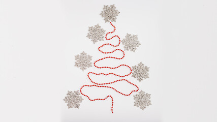Creative arrangement of snowflakes and red beads forming a Christmas tree shape on a white background, showcasing festive holiday spirit and seasonal decoration ideas
