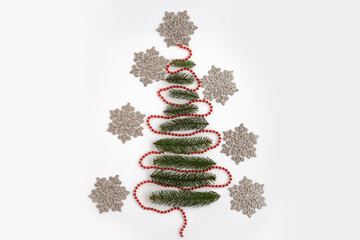Festive arrangement of green pine branches shaped like a Christmas tree, adorned with red beads and surrounded by decorative snowflakes, creating a holiday atmosphere